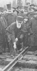 In this 1895 black and white photo, Donald Alexander Smith, surrounded by onlooking workers, bends low to swing the sledge hammer onto a railway spike set in the tie. This spike signalled the completion of a coast-to-coast rail system in Canada.